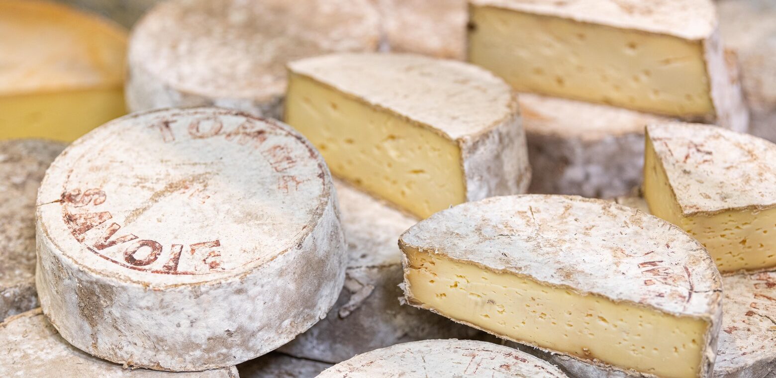 Meules de Tomme de Savoie exposées au Marché Pernoud, avec des tranches révélant un fromage à pâte pressée non cuite, typique de la région, offrant une texture crémeuse et un goût authentique.