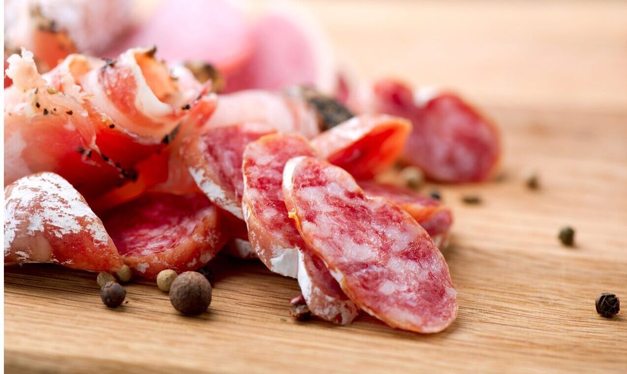 Tranches de saucisson artisanal, finement coupées, présentées sur une planche en bois au Marché Pernoud, mettant en avant la qualité et le savoir-faire de la charcuterie locale.