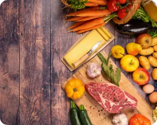 Assortiment de produits frais du Marché Pernoud, incluant des légumes colorés, un morceau de viande, du fromage savoyard et des pommes, disposés sur une table en bois rustique pour un repas authentique et local.